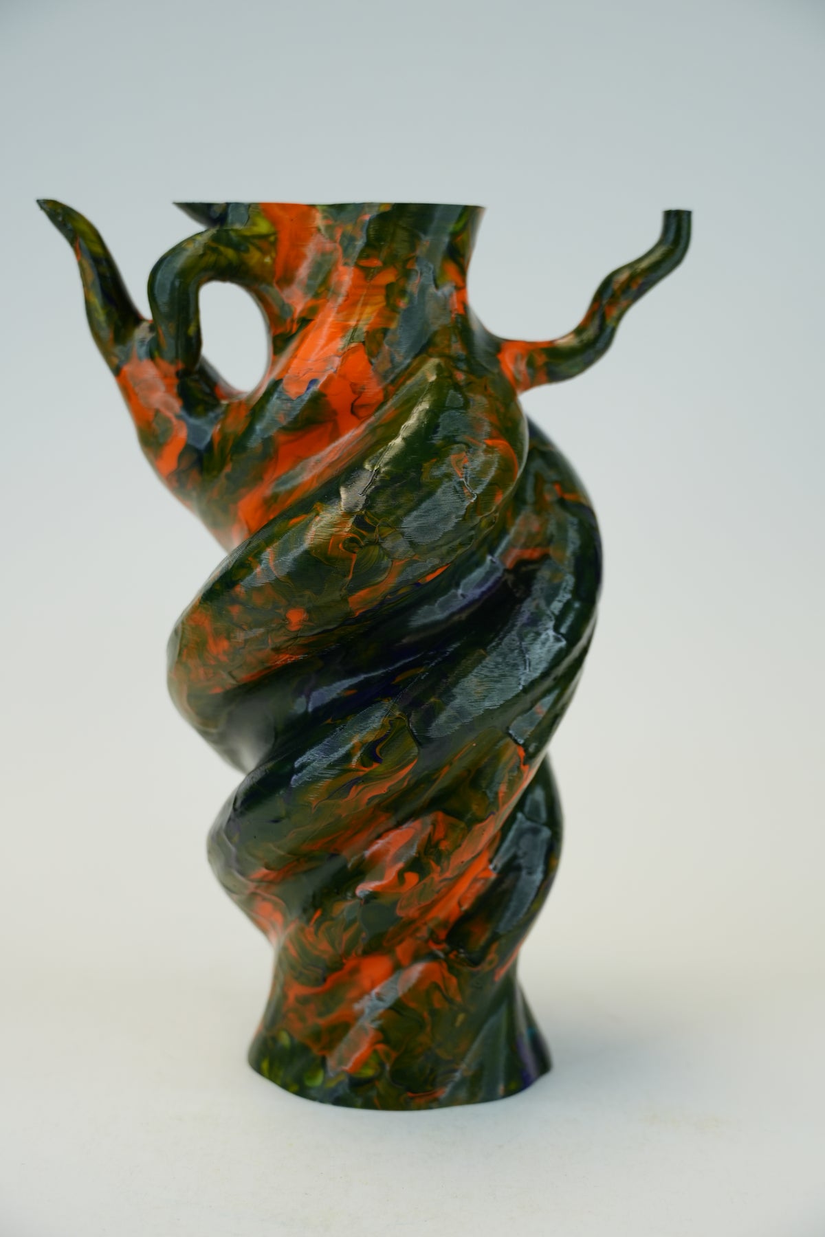 A sculptural spiral vase with a glossy marbled finish in black and burnt orange, photographed against a plain light gray studio background.