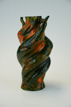 A sculptural spiral vase with a glossy marbled finish in black and burnt orange, photographed on a seamless light gray studio background.