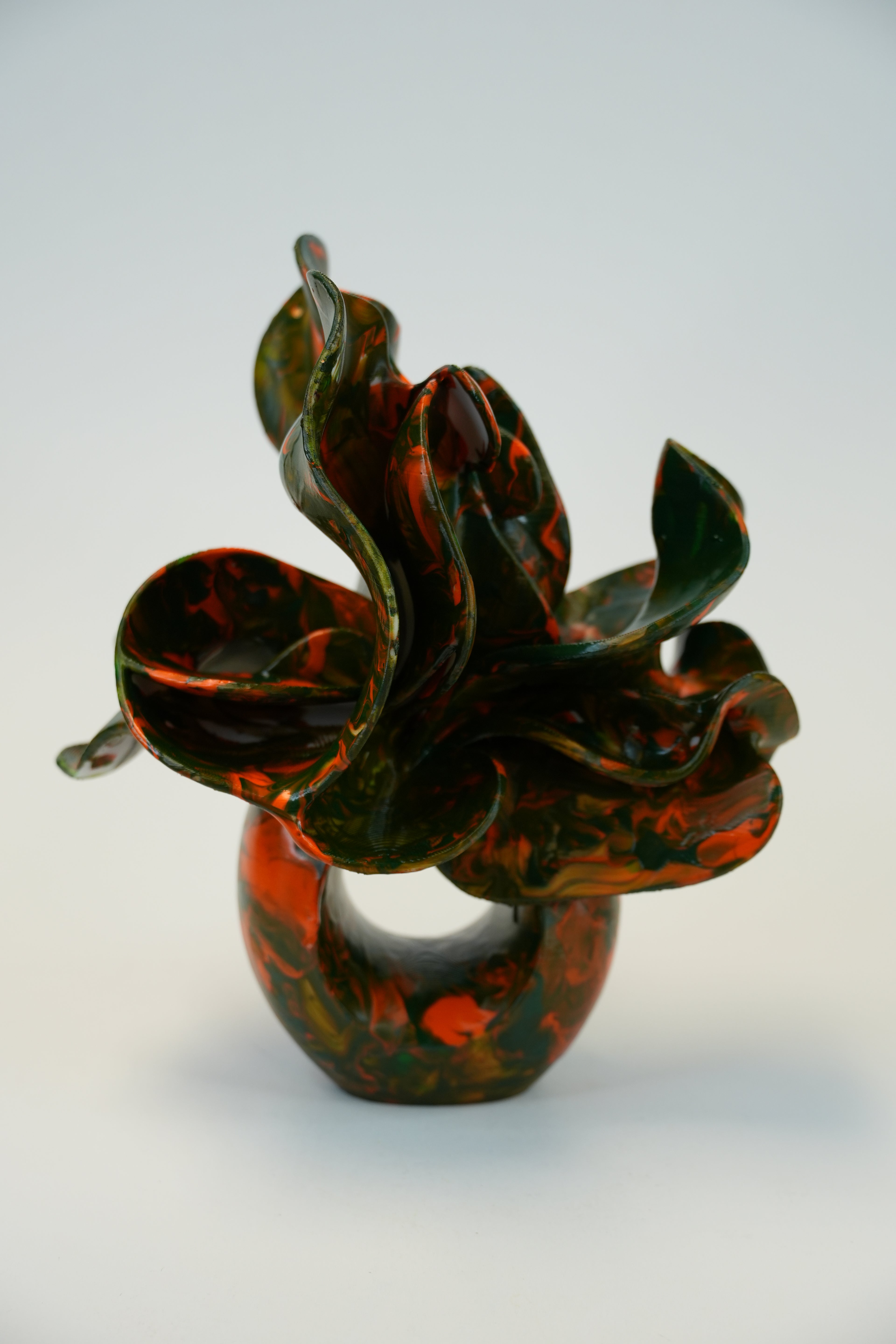 An abstract sculptural wall hook made of glossy, marbled dark green and burnt orange glass, mounted on a plain light gray wall.