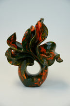An abstract sculptural vase with a glossy marbled pattern of deep green and burnt orange, photographed on a seamless light gray background.