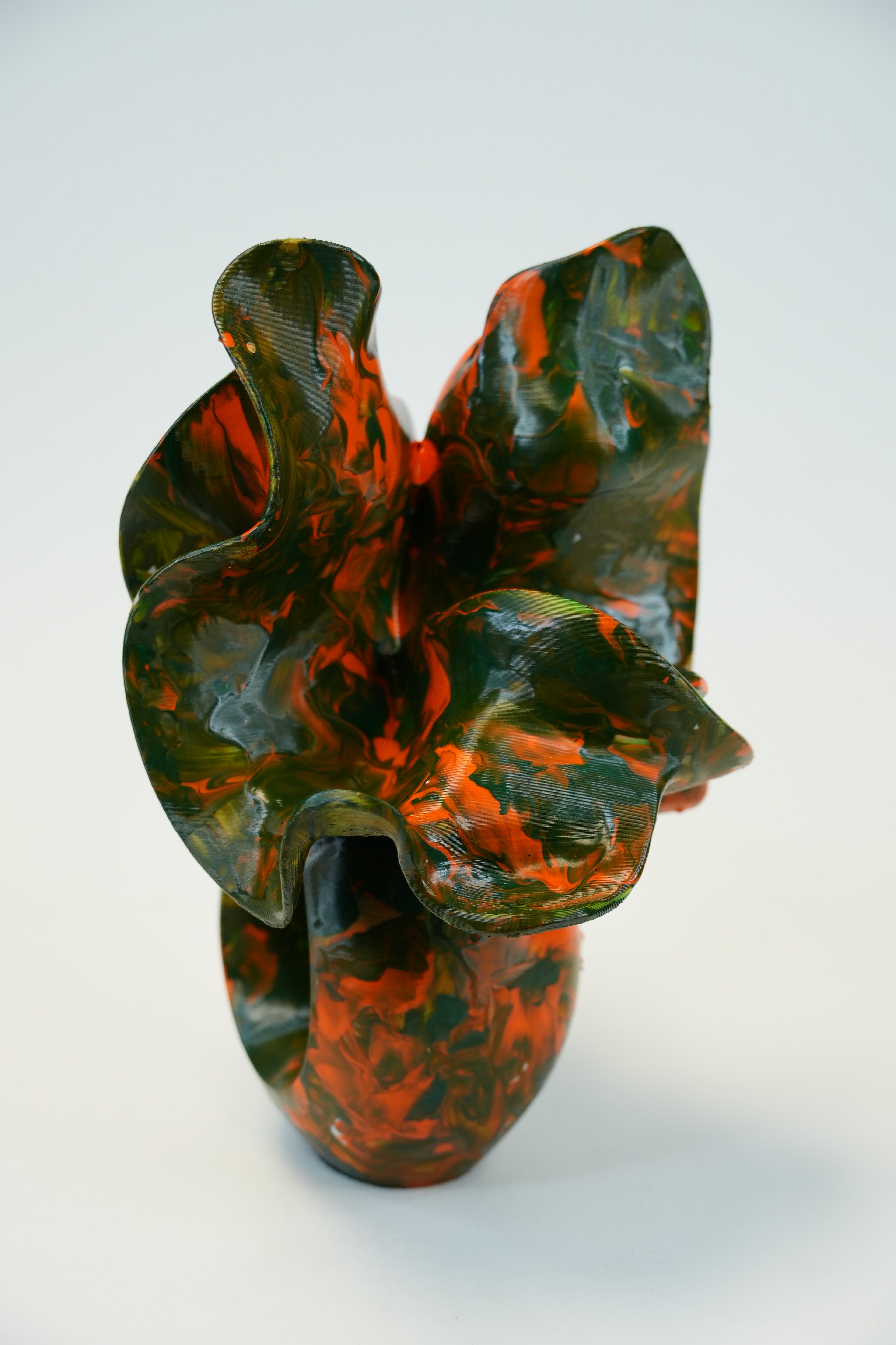A sculptural, organic-shaped vase with a glossy marbled pattern of dark green and burnt orange, photographed against a clean white background.