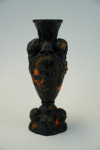 A vintage decorative glass vase with a dark black and amber-orange marbled pattern, photographed against a plain light gray background.