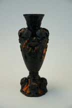 A dark glossy decorative object with a bulb-shaped center, flared rim, and sculpted ends, shown against a plain light background.