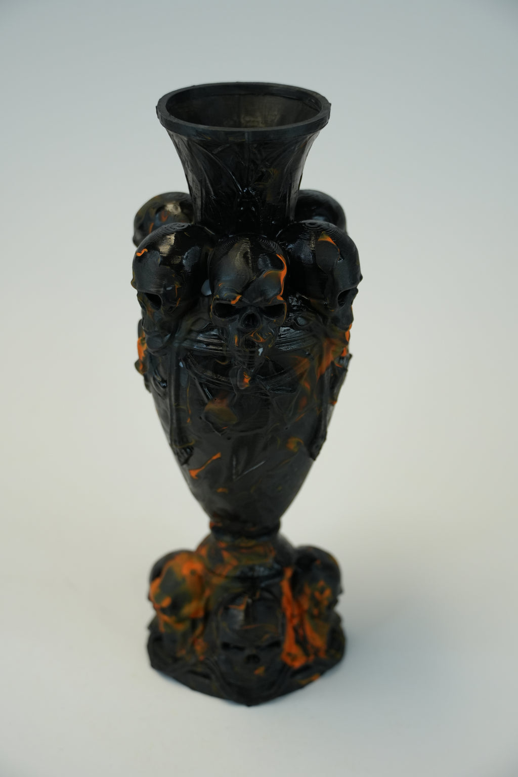 A black glass vase decorated with sculpted skulls and orange marbled accents, set against a plain light gray background.