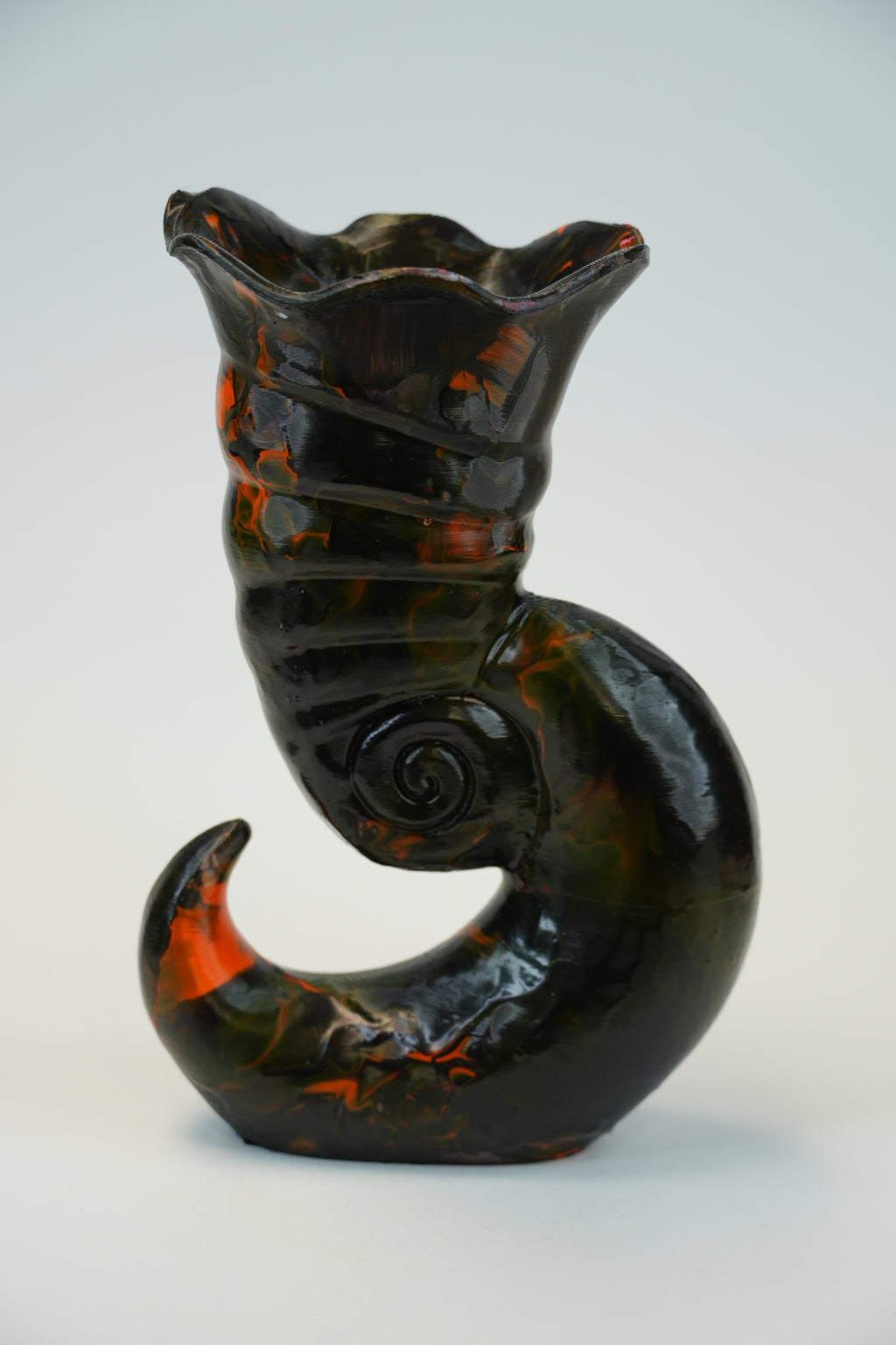 A sculptural ceramic vase with a glossy black glaze and vibrant orange and brown marbled accents, photographed against a neutral light gray background.