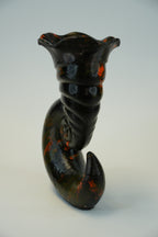 A glossy black ceramic lobster figurine with orange and blue speckled accents, mounted on a plain light gray wall.