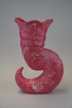 A sculptural ceramic vase shaped like a curled shell or spiral shell, in a glossy pink glaze with white marbled veining, photographed against a neutral gray studio background.