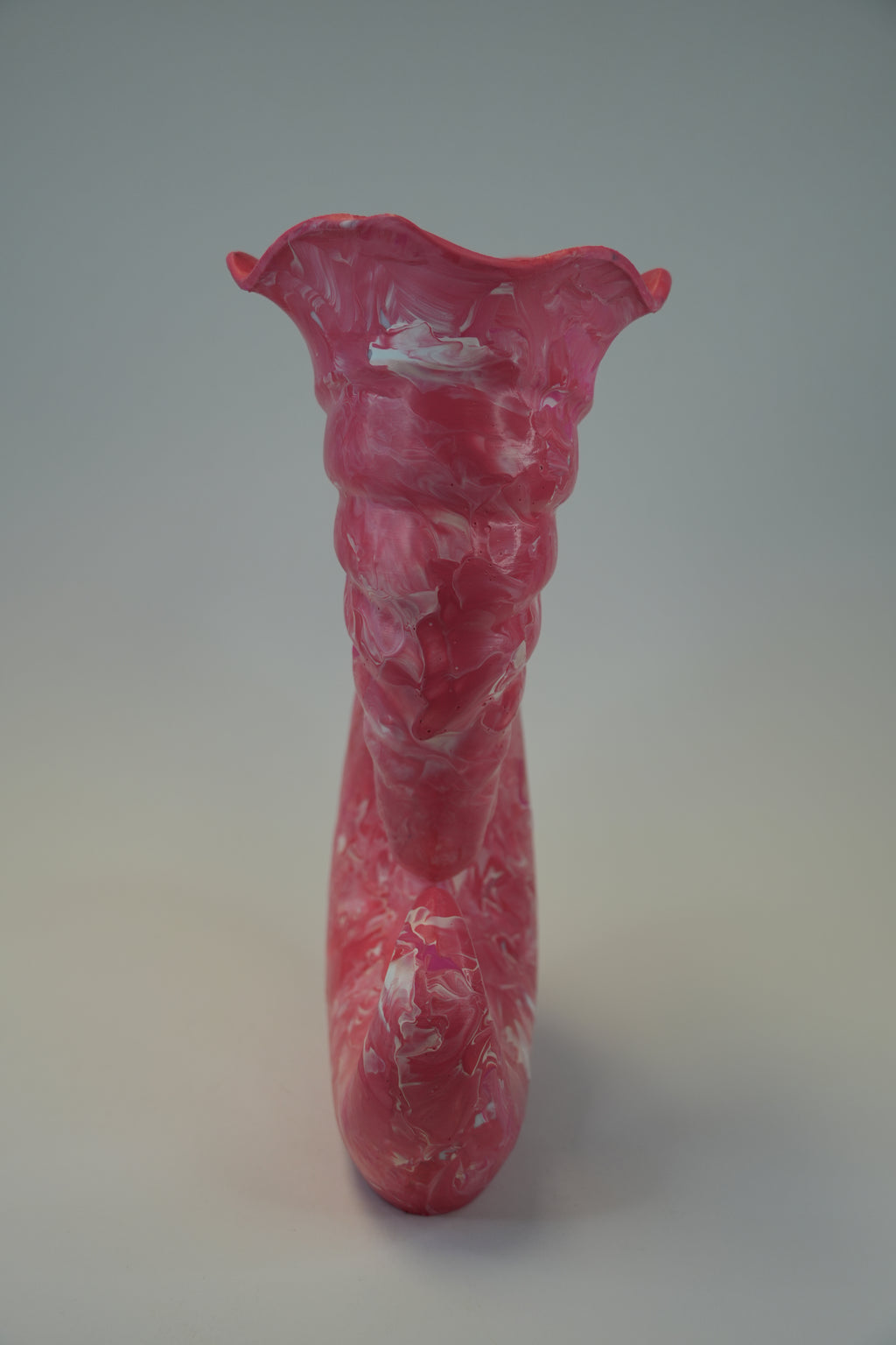 A sculptural ceramic vase with a flared, organic top and a bulbous neck, featuring a pink and white marbled or swirled glaze, photographed against a neutral gray background.
