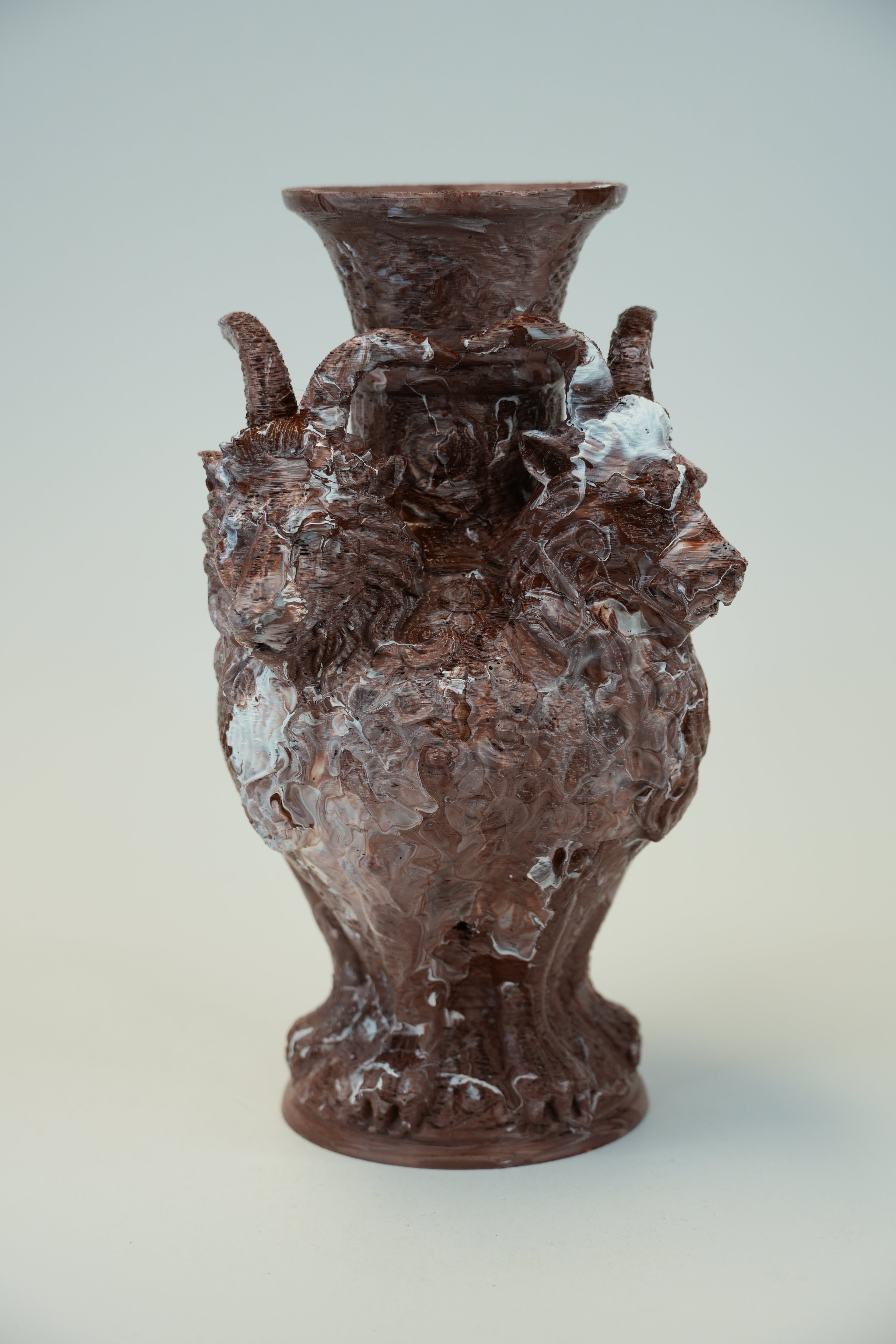 A sculptural ceramic vase with a highly textured, organic, and bubbled surface in earthy brown and terracotta tones, mounted on a plain light gray wall.