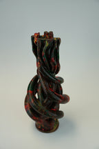 A sculptural twisted vase with a glossy finish, featuring a marbled pattern of black, deep green, and red, set against a plain light gray background.