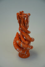 An abstract sculptural vase with a twisted, organic coiled design in terracotta orange and white marbled clay, standing on a circular base against a neutral light gray background.