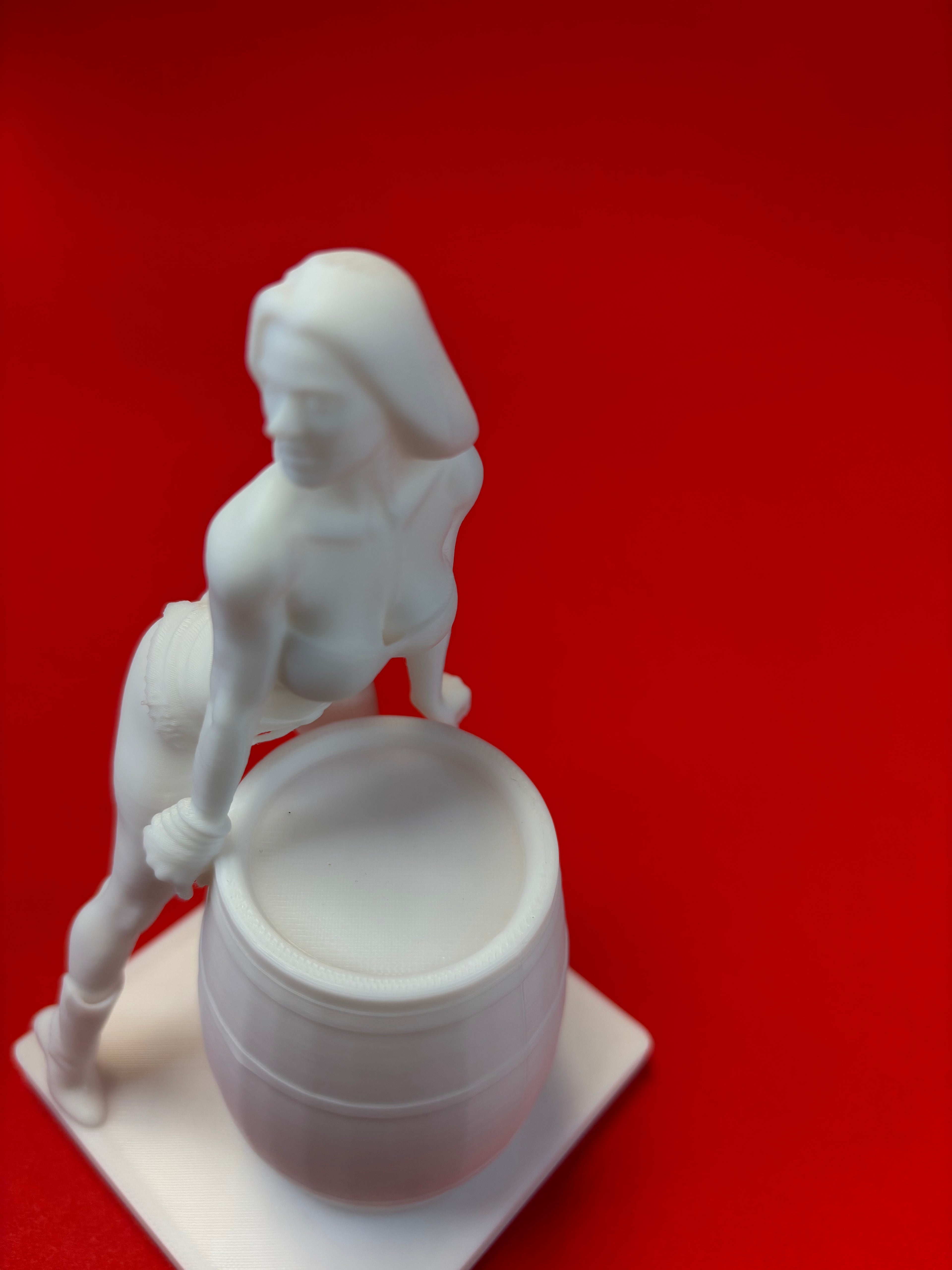 White sculpture of a figure holding a barrel against a red background