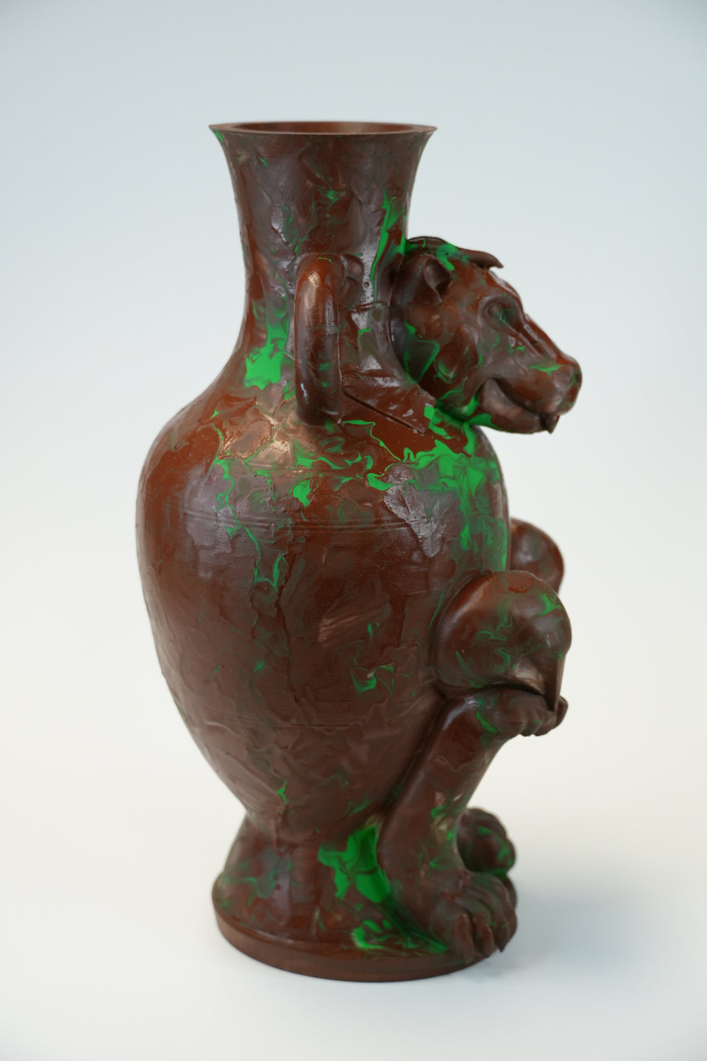 A sculptural brown vase with a dog figure integrated into the body, featuring distressed green patina-like patches, photographed against a clean white studio background.