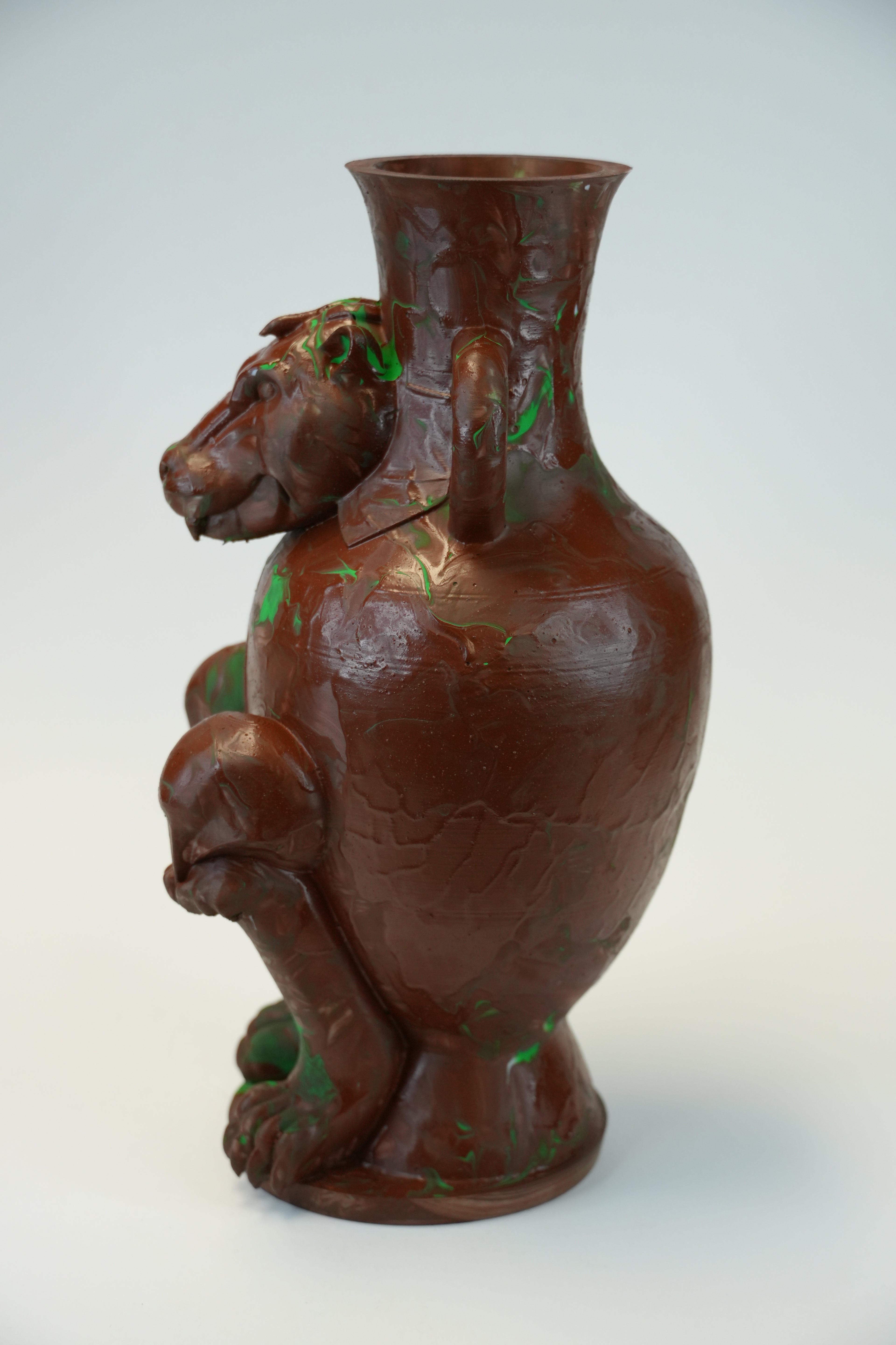 A sculptural brown ceramic vase shaped like a seated animal figure, with small green painted accents and a flared neck, photographed against a plain light background.