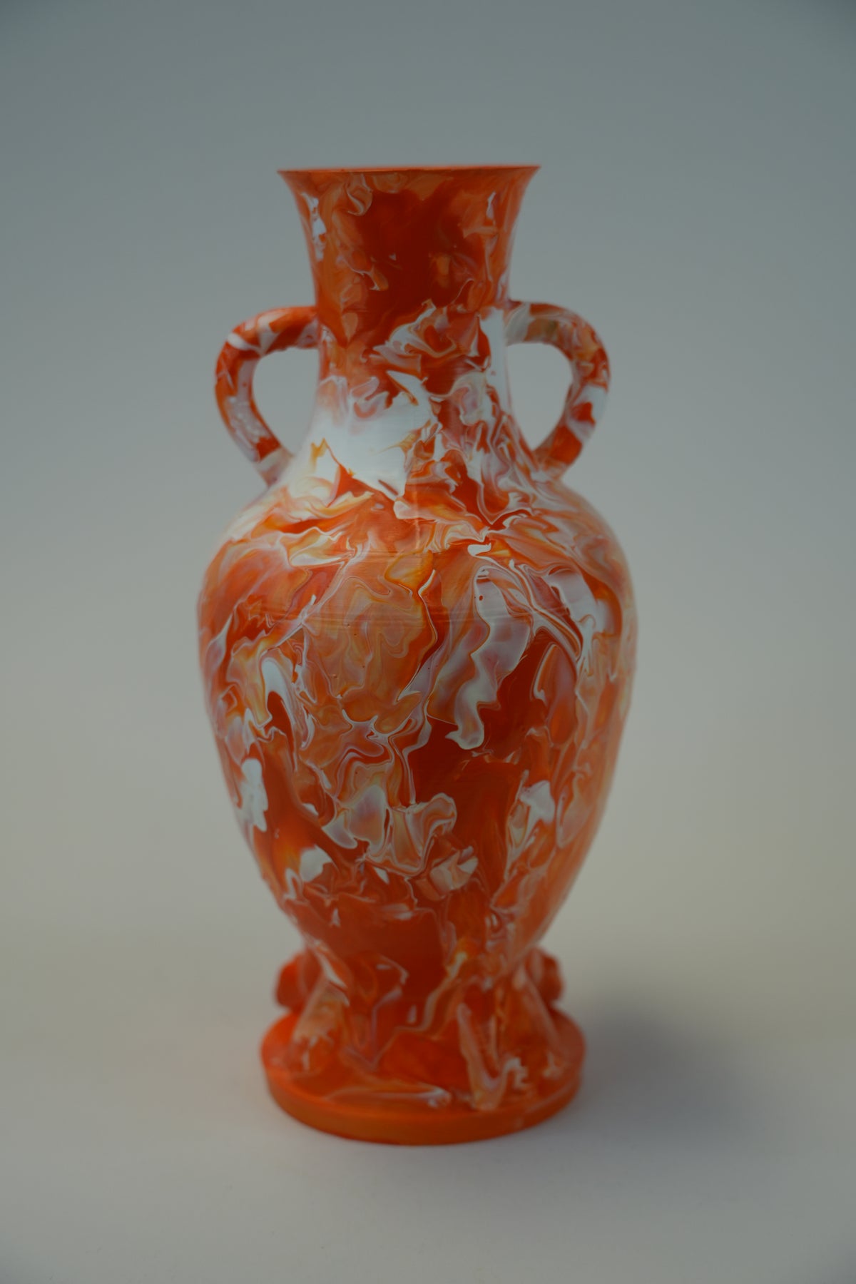 An orange and white marbled ceramic vase with two side handles and a flared rim, photographed against a plain light gray background.