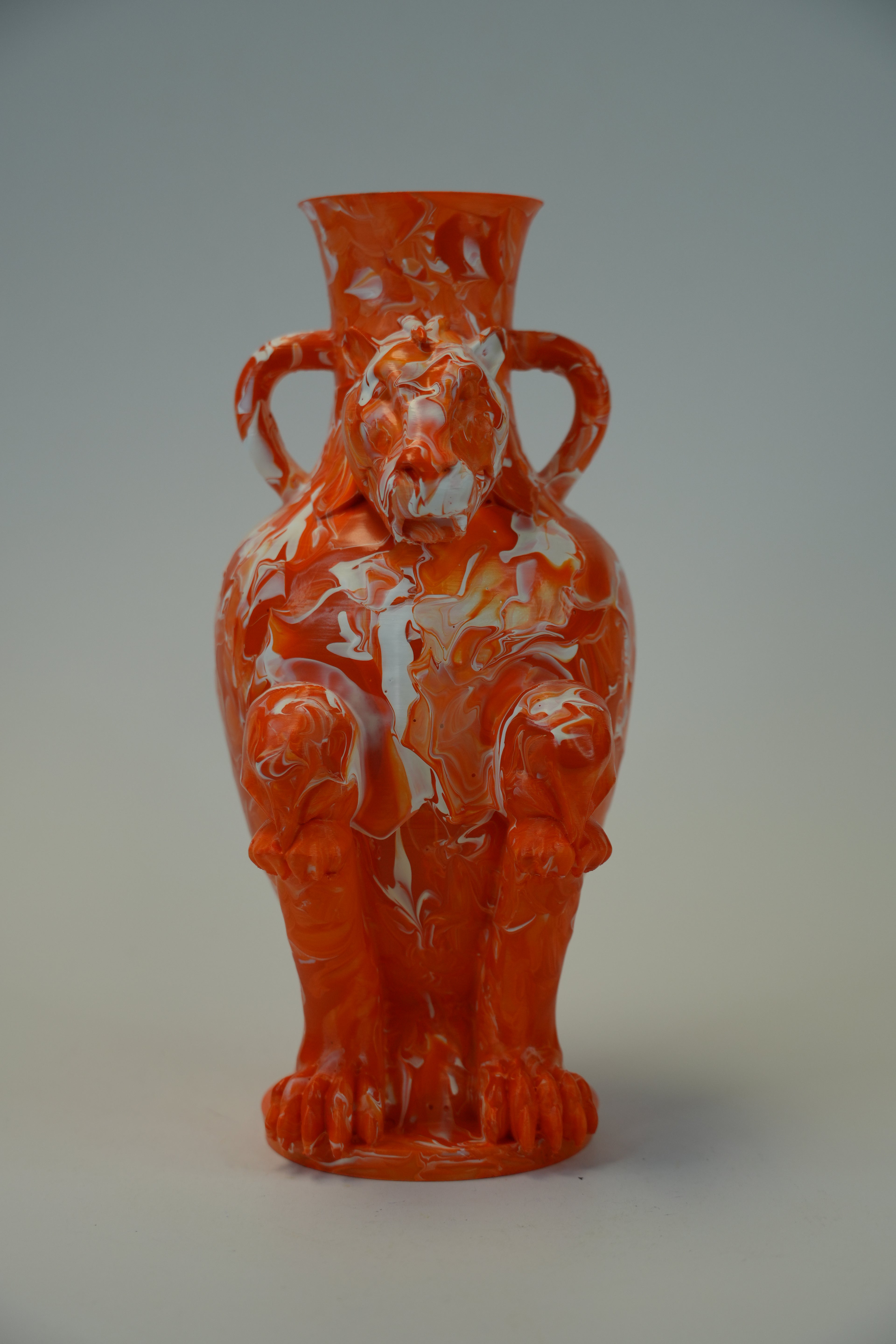 An orange ceramic vase sculpted in the shape of a seated tiger, featuring white marbled swirls throughout and two side handles, set against a neutral gray background.