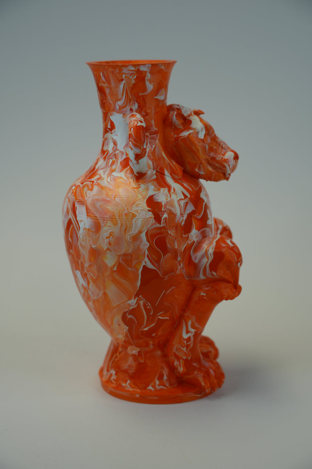An orange and white marbled glass vase shaped like a crouching bear, photographed against a neutral light gray background.