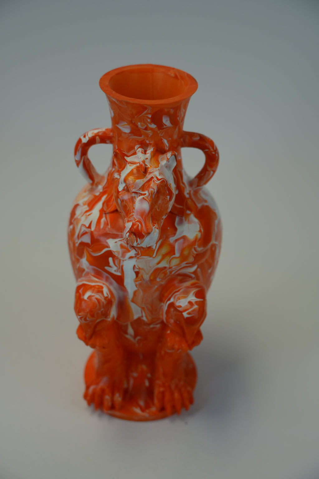 An orange ceramic vase with a sculpted, headed animal or dragon-like figure and two side handles, shown on a neutral gray background.