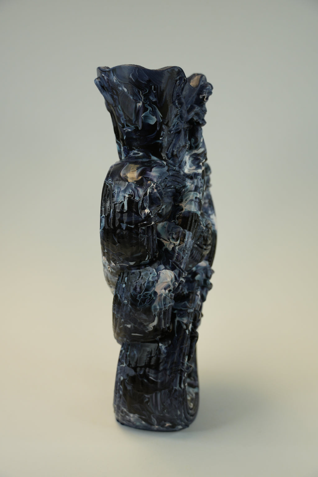 A dark, textured abstract sculpture or decorative object with swirling black, gray, and white marbled patterns, photographed against a plain light beige wall.