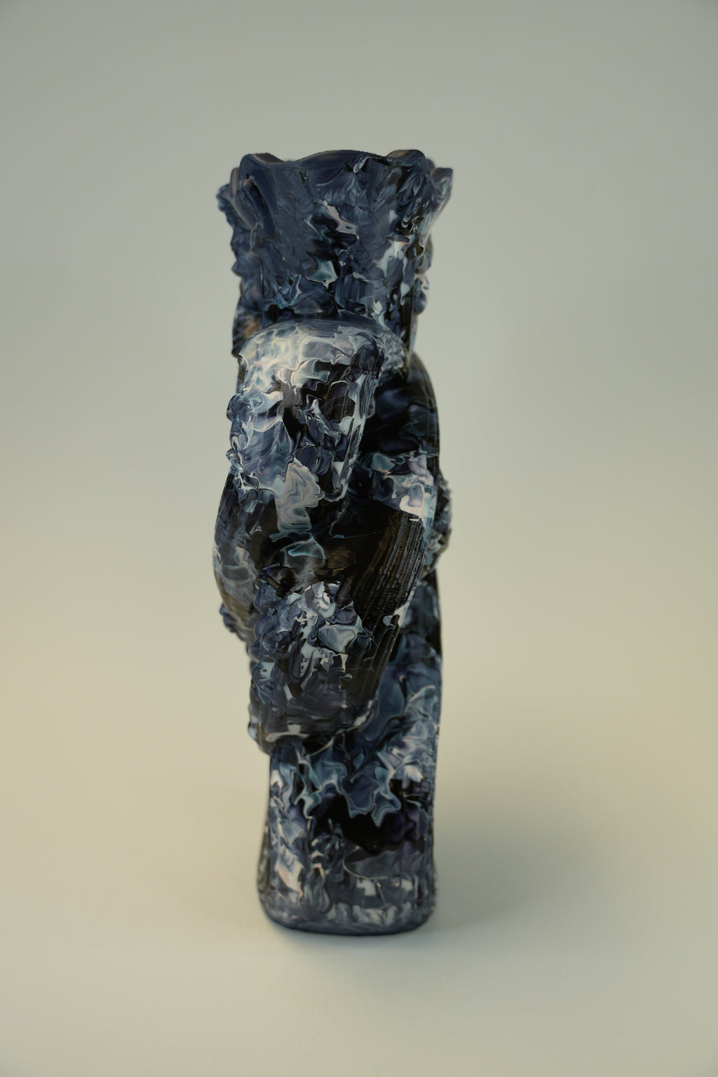 A small sculptural figurine of a stylized bird or creature in dark blue, black, and white marbled stone or resin, photographed against a plain light gray studio background.