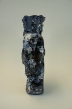 A small sculptural figurine of a stylized bird or creature in dark blue, black, and white marbled stone or resin, photographed against a plain light gray studio background.