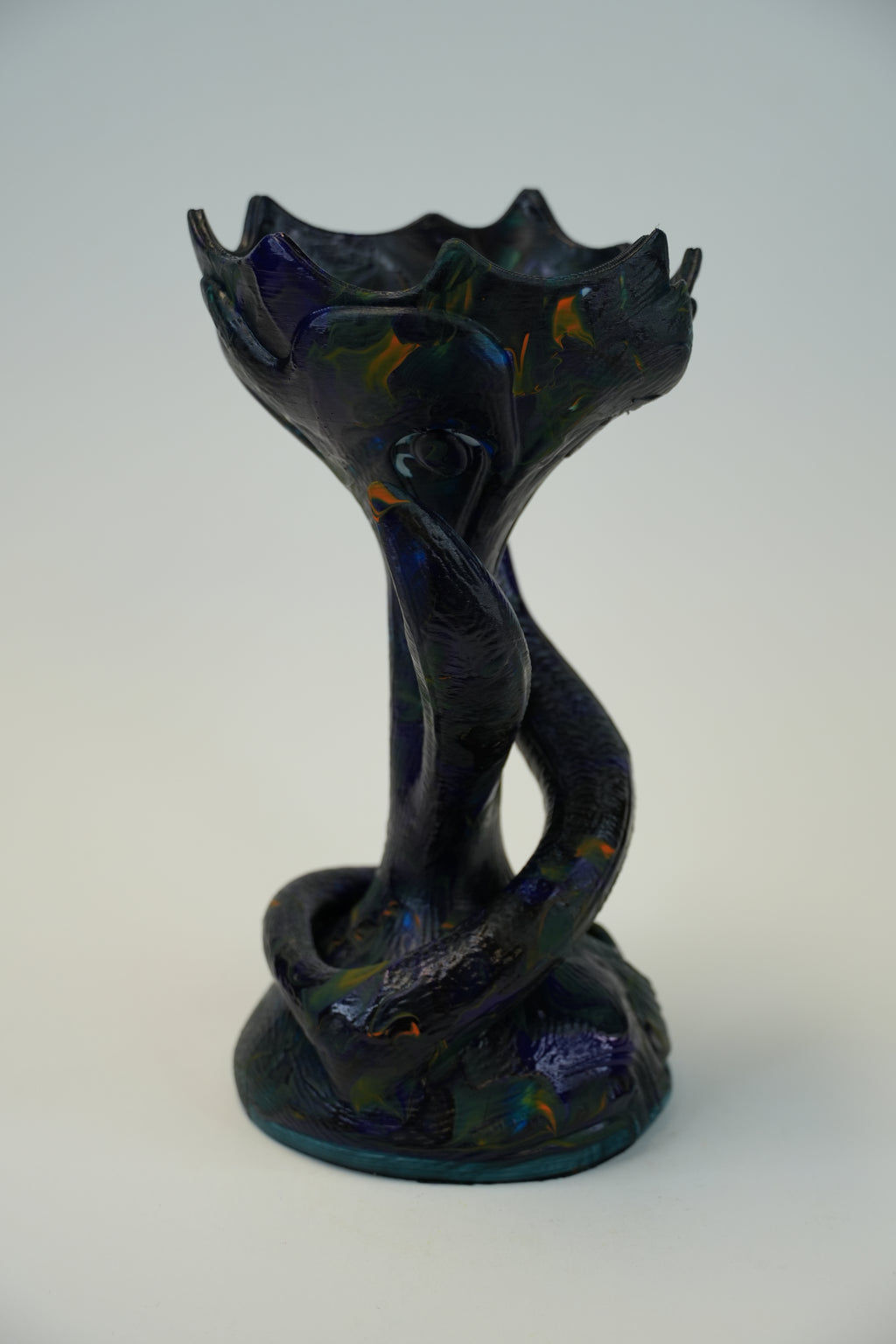 A sculptural ceramic vase with a coiled snake motif and a lotus-like flared rim, shown on a plain light gray studio background. The glaze is predominantly very dark blue-black with iridescent blue, purple, and warm gold reflections.
