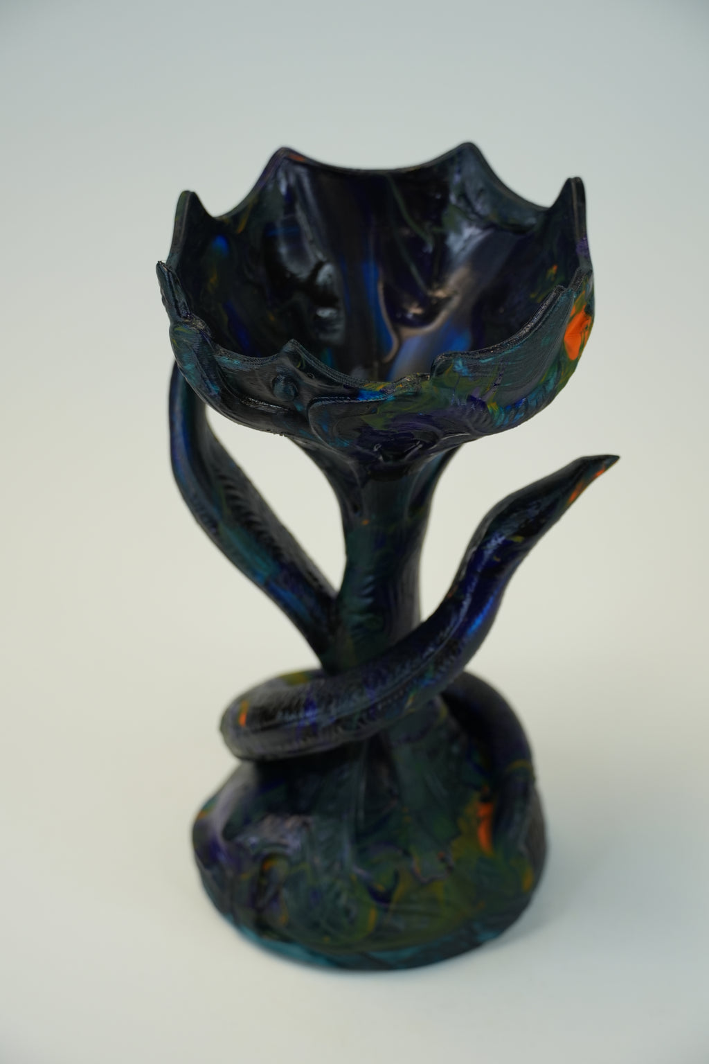 A sculptural ceramic vase with a lotus flower shape, featuring a glossy dark blue and black glaze with subtle iridescent green and orange reflections, set against a plain light gray background.