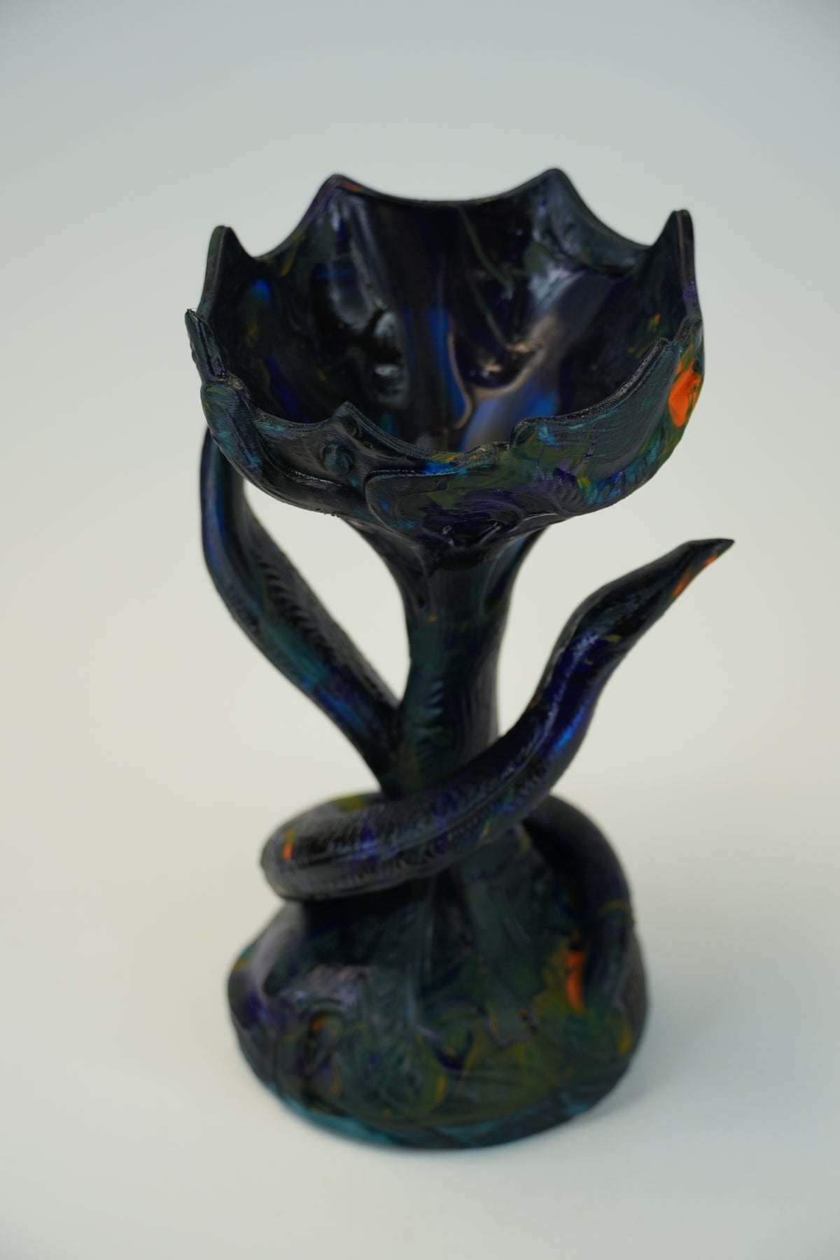 A sculptural ceramic vase with a lotus flower shape, featuring a glossy dark blue and black glaze with subtle iridescent green and orange reflections, set against a plain light gray background.