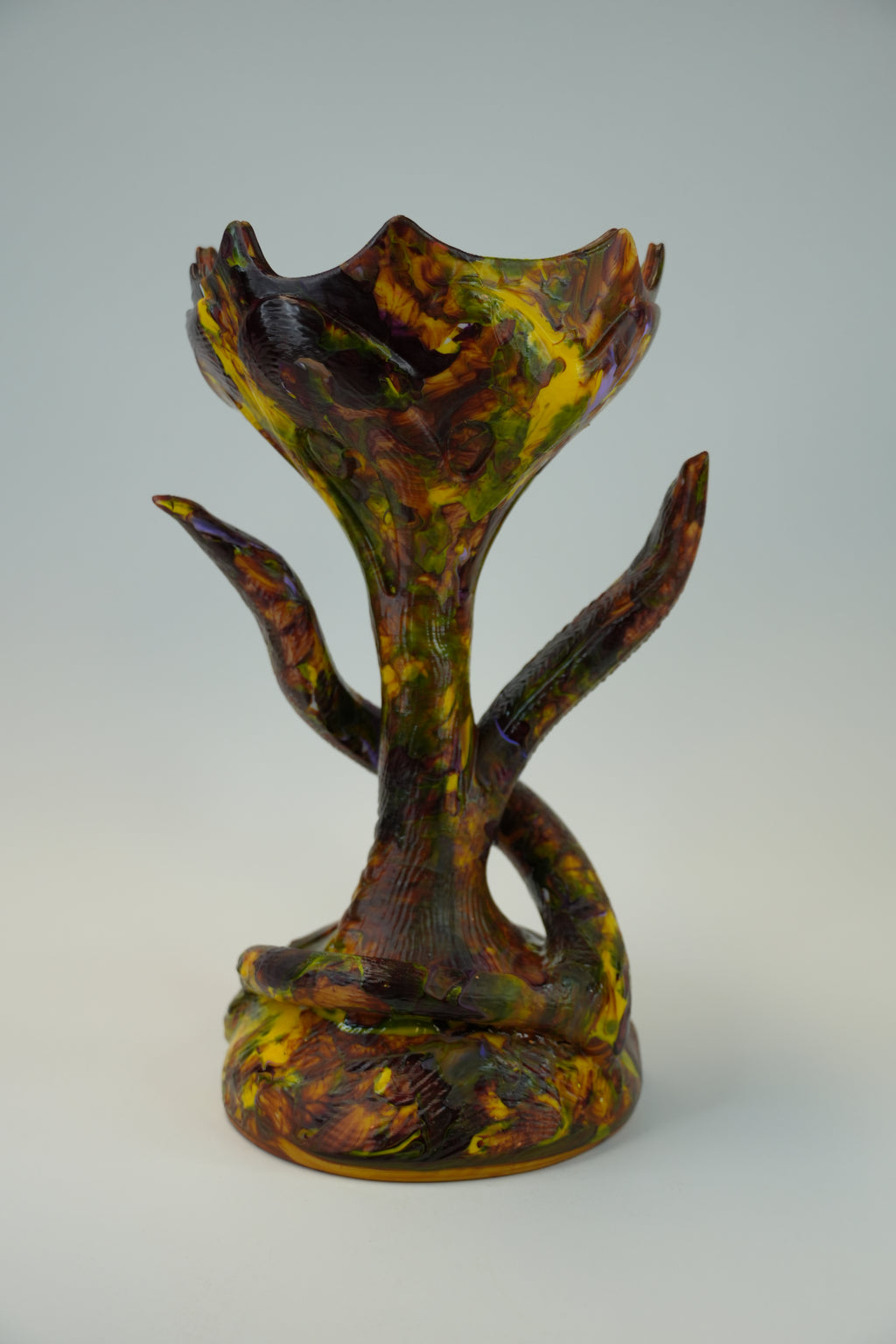 A sculptural ceramic vase with a mushroom-like form, featuring a marbled pattern of yellow, green, and dark brown glaze on a light gray background.