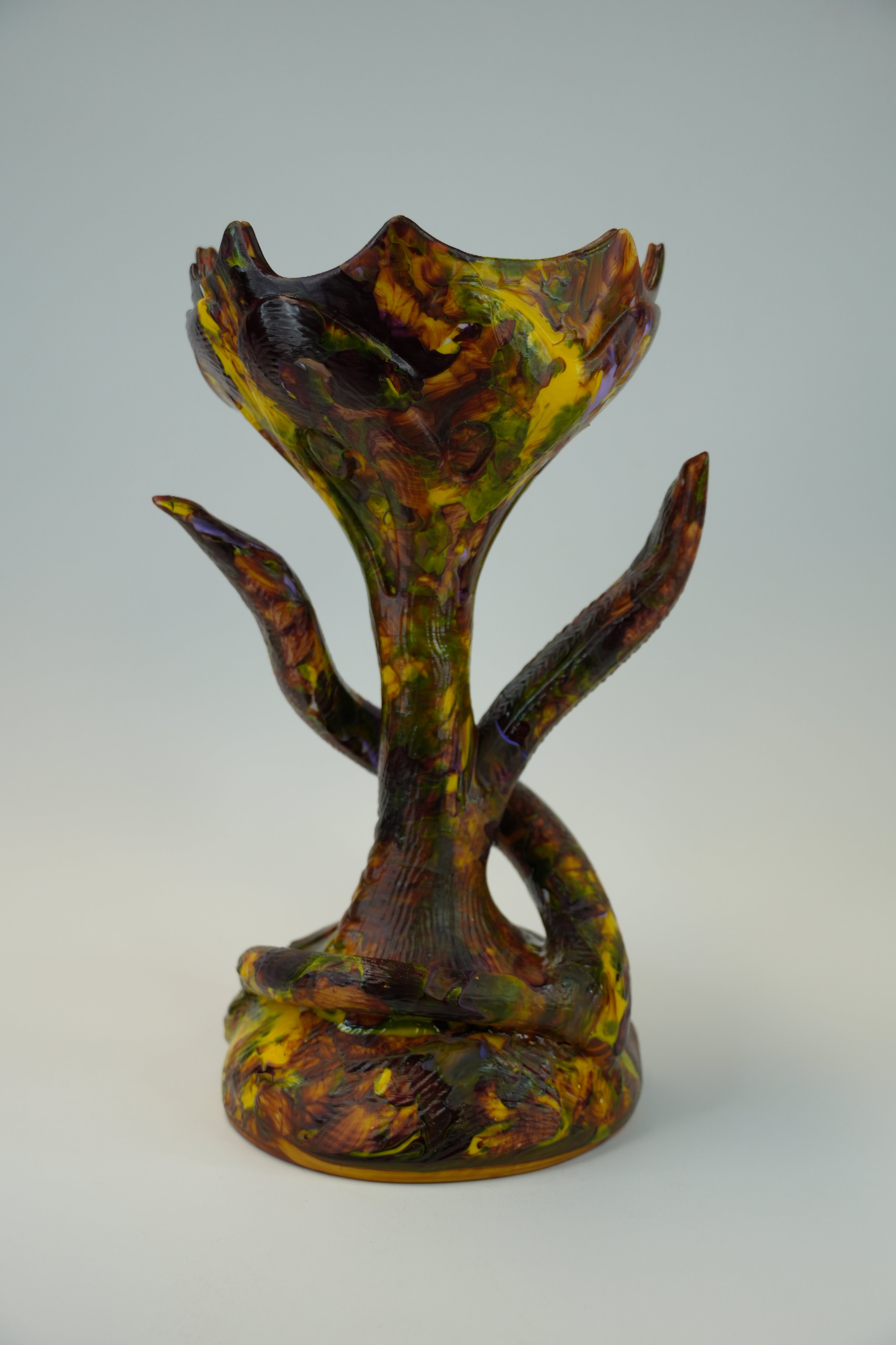 A sculptural ceramic vase with a mushroom-like form, featuring a marbled pattern of yellow, green, and dark brown glaze on a light gray background.