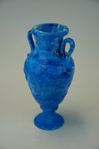 A small blue ceramic vase with a textured, marbled finish, featuring two handles and a flared base, set against a plain light gray background.