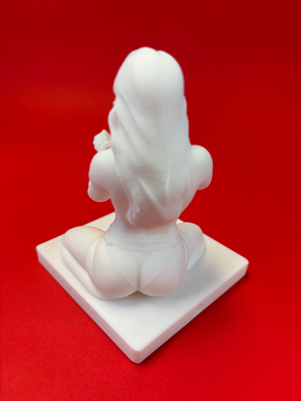 White sculpture of a seated figure on a red background